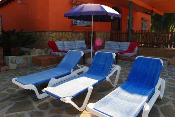 A patio with three blue lounge chairs and a purple umbrella.
