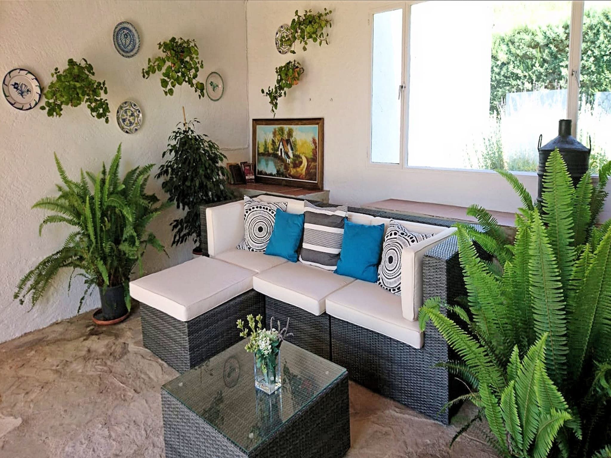 Een gezellige woonkamer met een hoekbank, een glazen bijzettafeltje en verschillende potplanten.