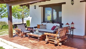 A covered outdoor seating area with a sofa and chairs, a glass table, and lanterns. - Beautiful villa in Andalusia near the forest (La Joya)