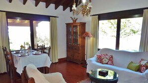 A dining area with a table set for four, a sofa with floral cushions, and a wooden cabinet. - Beautiful villa in Andalusia near the forest (La Joya)