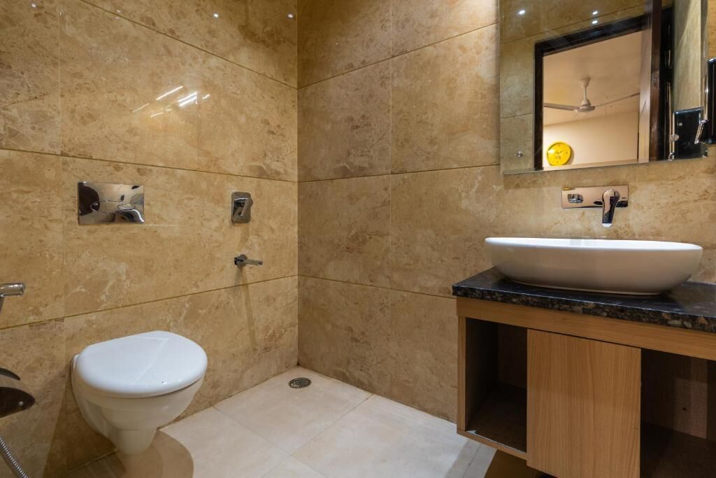 Une salle de bain avec des toilettes blanches, un lavabo avec un miroir au-dessus et un espace douche.