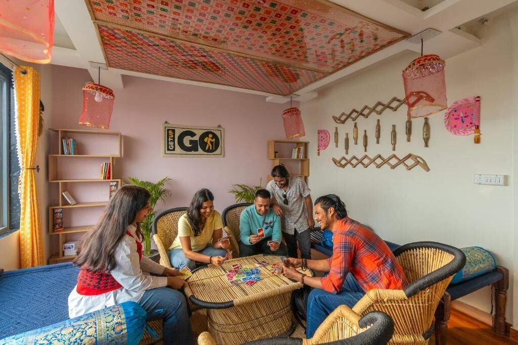 A group of people playing cards in a room with a patterned ceiling, wicker furniture, and shelves with books.