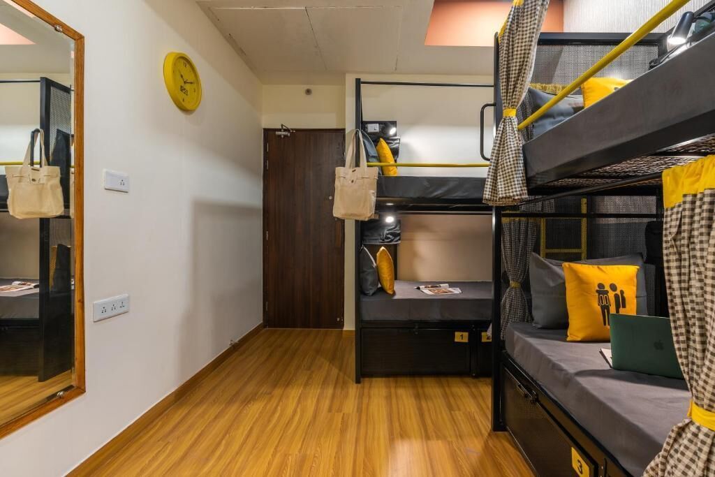 A bunk bed room with a wooden floor, a clock on the wall, and a suitcase on the bed.