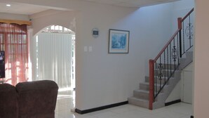 A spacious living area with a staircase, a framed picture on the wall, and a window with curtains. - Lush oasis in port of Spain with private pool (Port of Spain)