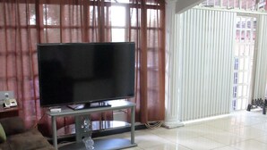 A living room with a large flat-screen TV on a stand, a brown sofa, and a coffee table with a remote control. - Lush oasis in port of Spain with private pool (Port of Spain)