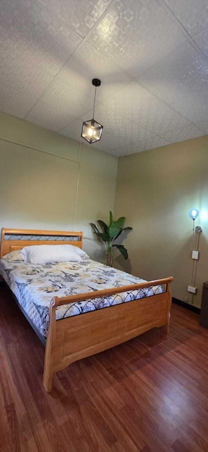 A bedroom with a wooden bed, a hanging light fixture, a potted plant, and a bedside lamp. - Lush oasis in port of Spain with private pool (Port of Spain)