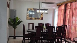 A dining area with a round table, six chairs, a hanging plant, a large mirror, and a window with red curtains. - Lush oasis in port of Spain with private pool (Port of Spain)