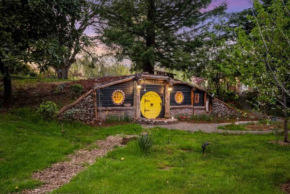 A rustic hobbit-style house with a large yellow door, surrounded by greenery and trees.