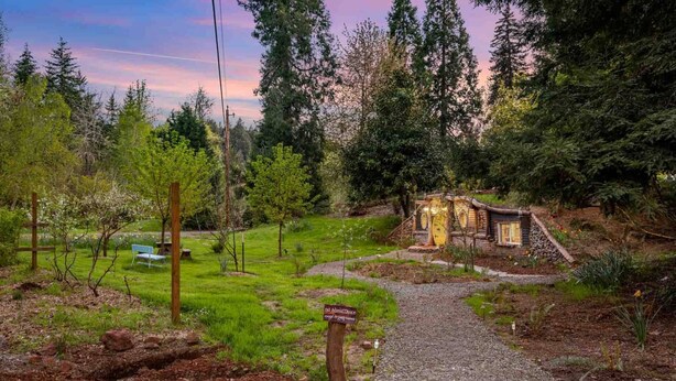 A rustic cabin surrounded by a lush garden, with a gravel path leading to it. - Enchanting and Fantastical Hobbit Home, *Pet Friendly*, Steps from Creeks, Pond, and Waterfall (Salem)