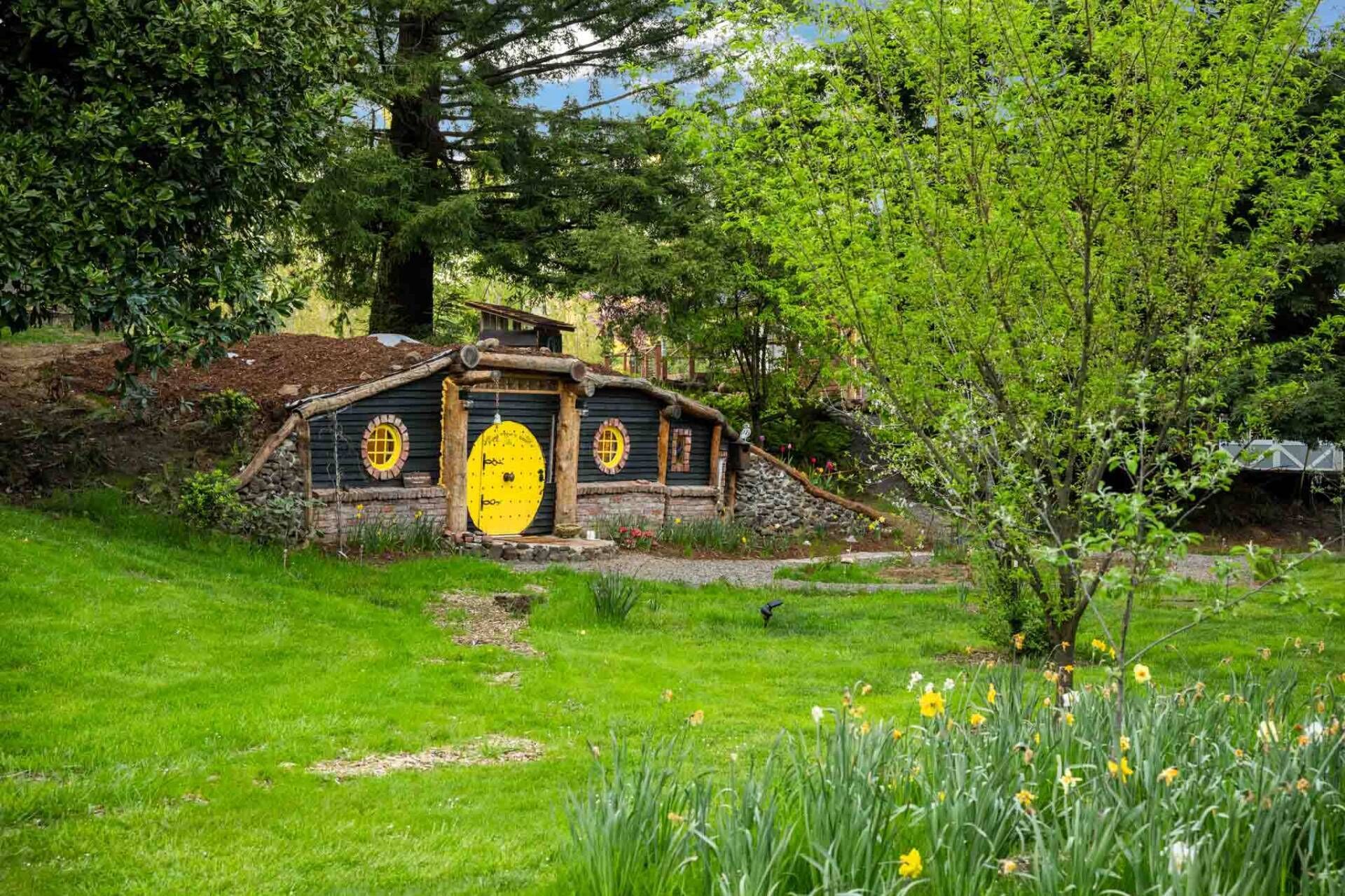 A Hobbit-style house with a yellow door, surrounded by lush greenery and daffodils.