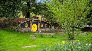A Hobbit-style house with a yellow door, surrounded by lush greenery and daffodils.