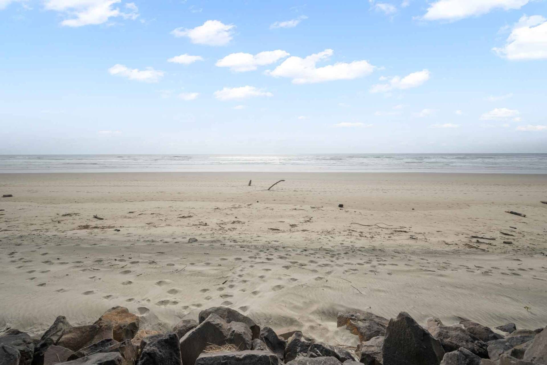 A beach with a rocky foreground and a calm sea under a clear sky.