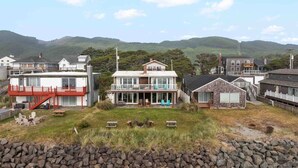 A coastal residential area with multiple houses, including a prominent two-story house with a balcony and a smaller adjacent house.