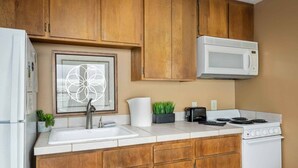 A kitchen with wooden cabinets, a white sink, a microwave, a stove, and a framed artwork above the sink.