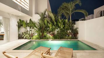 A poolside area with two wicker lounge chairs, a pool, and lush tropical plants.