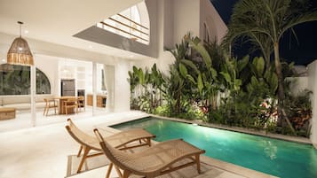 A modern indoor pool area with lounge chairs, a dining area, and lush tropical plants.