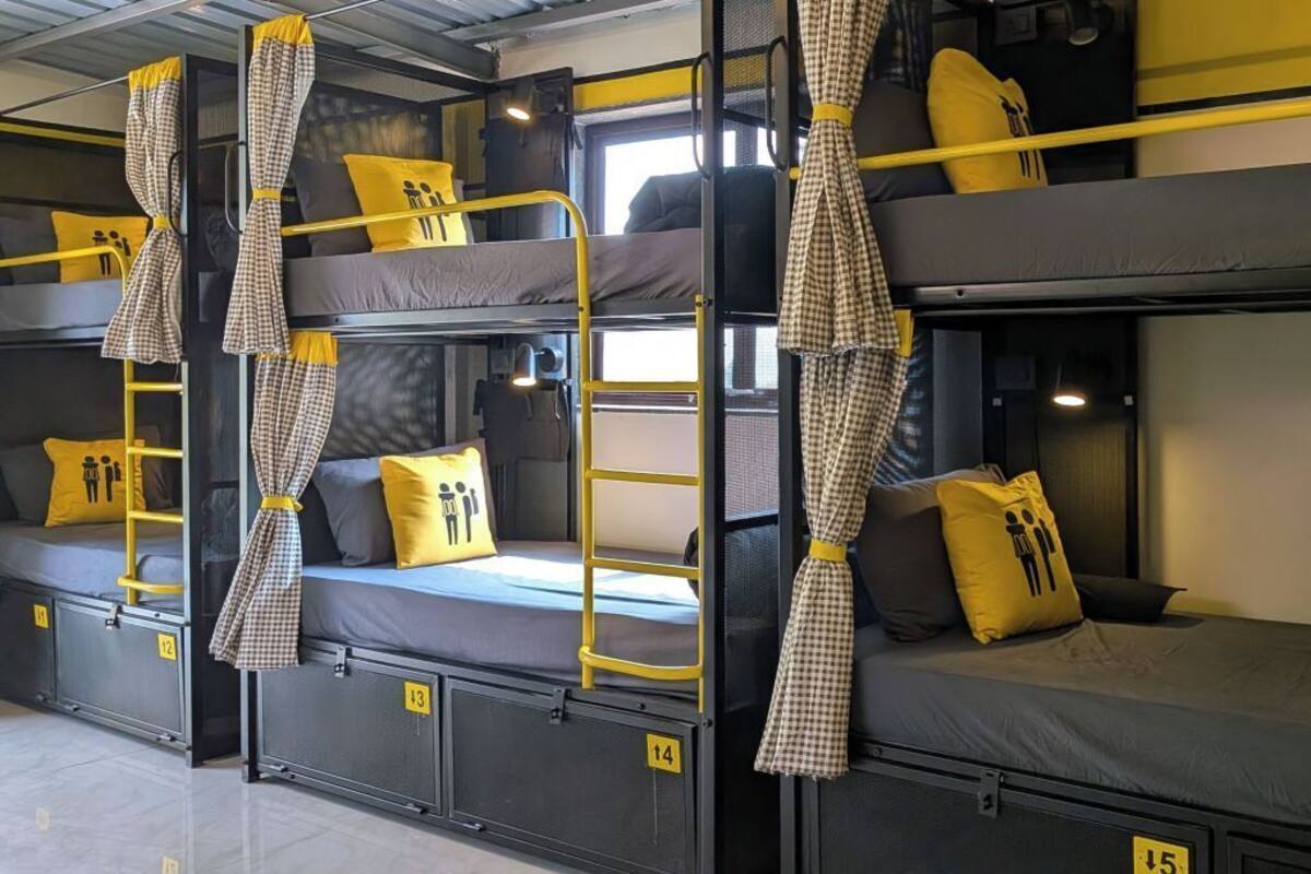 A dormitory-style room with bunk beds, each with a number tag, and checkered curtains.