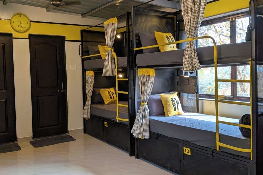 A dormitory room with bunk beds, a clock, and a window with curtains.