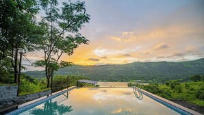 An infinity pool with a view of a lake and mountains during sunset. - The Hosteller Panshet, Lakeview  (Pune)