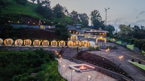 A series of circular structures with a fire feature in the center, surrounded by a landscaped area with steps leading up to a building. - The Hosteller Panshet, Lakeview  (Pune)