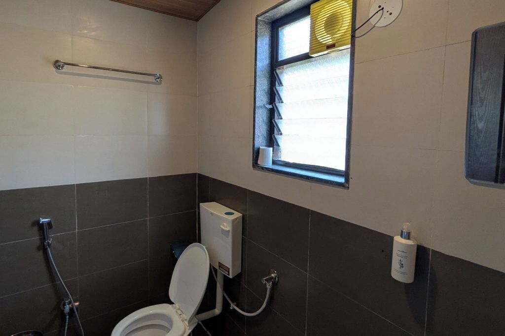 Une salle de bain équipée de toilettes, d’un sèche-mains, d’une fenêtre avec stores et d’un porte-serviettes.