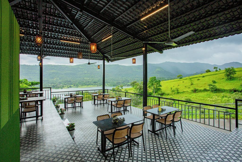 Una terraza al aire libre con mesas y sillas, con vistas a un paisaje verde exuberante y un lago.