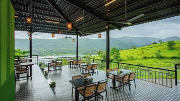 Una terraza al aire libre con mesas y sillas, con vistas a un paisaje verde exuberante y un lago.