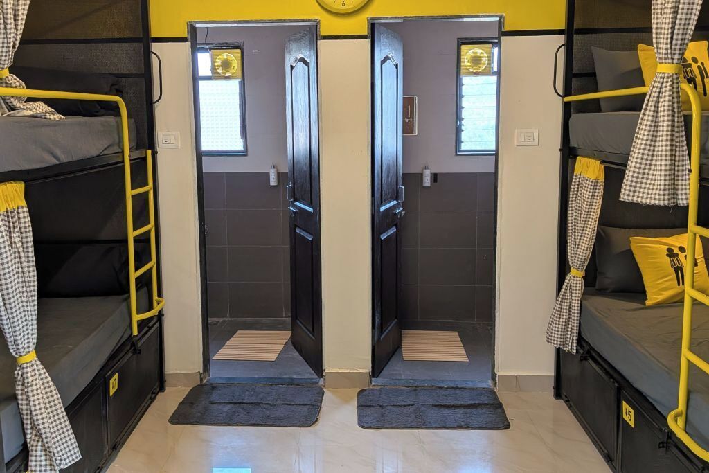 A dormitory room with bunk beds, a door with a window, and a small clock on the wall.