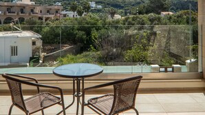 A terrace with two wicker chairs and a table, overlooking a hillside with buildings and greenery. - Altirina Studios (Almyrida)