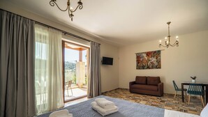 A hotel room with a bed, a sofa, a TV, and a dining area with chairs and a table. - Altirina Studios (Almyrida)
