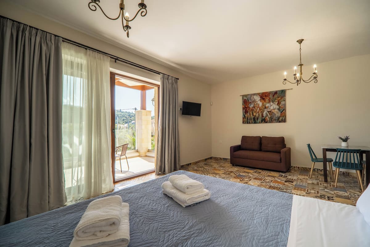 A hotel room with a bed, a sofa, a TV, and a dining area with chairs and a table.