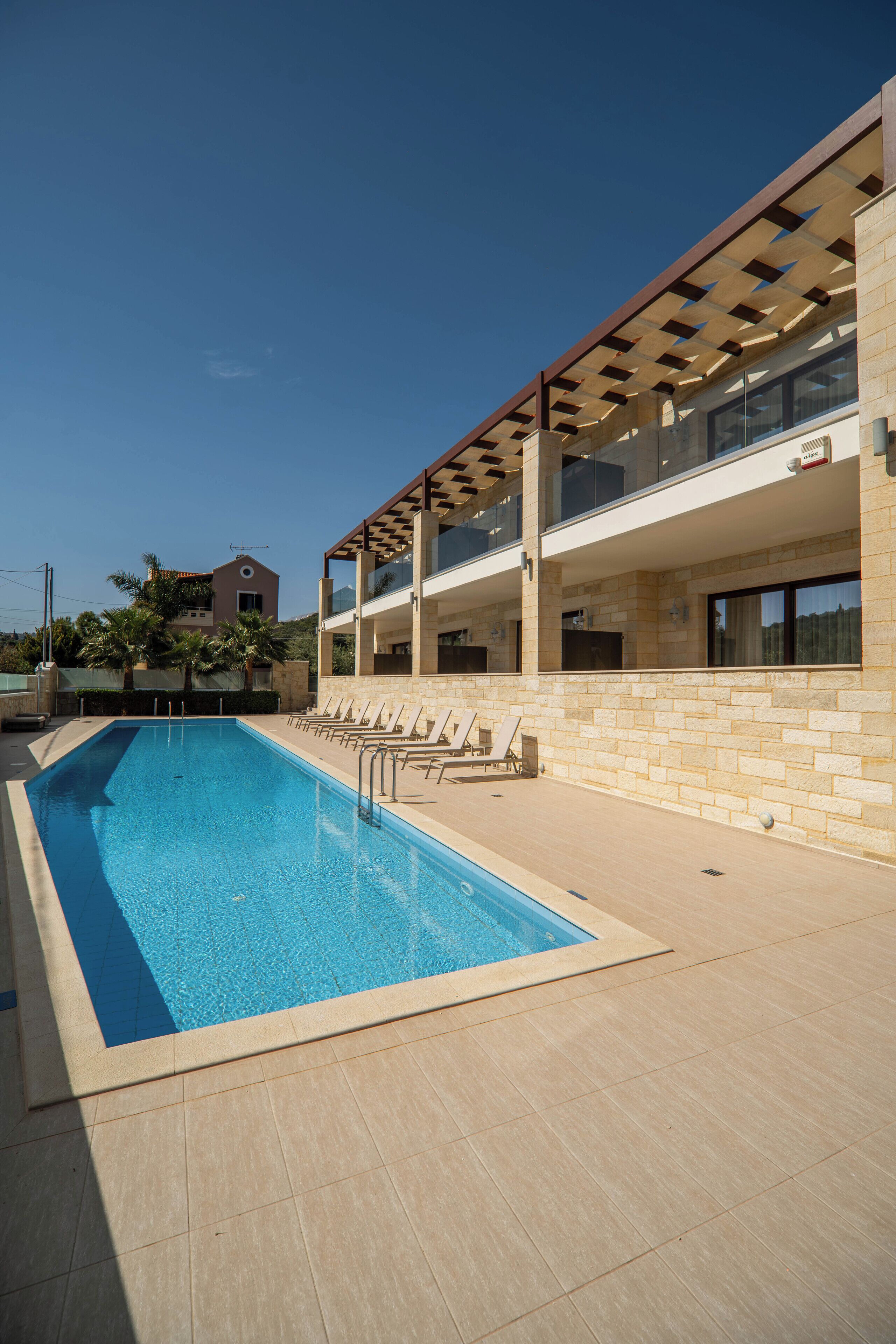 A swimming pool with sun loungers, a covered seating area, and a building with balconies.