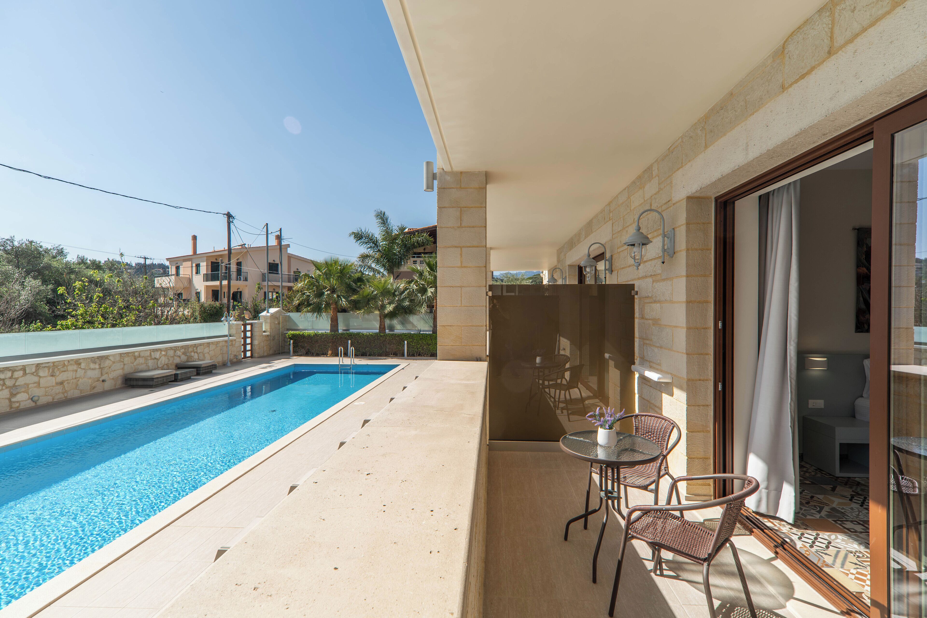 A swimming pool with a patio area, including a table and chairs, and a view of the surrounding buildings.