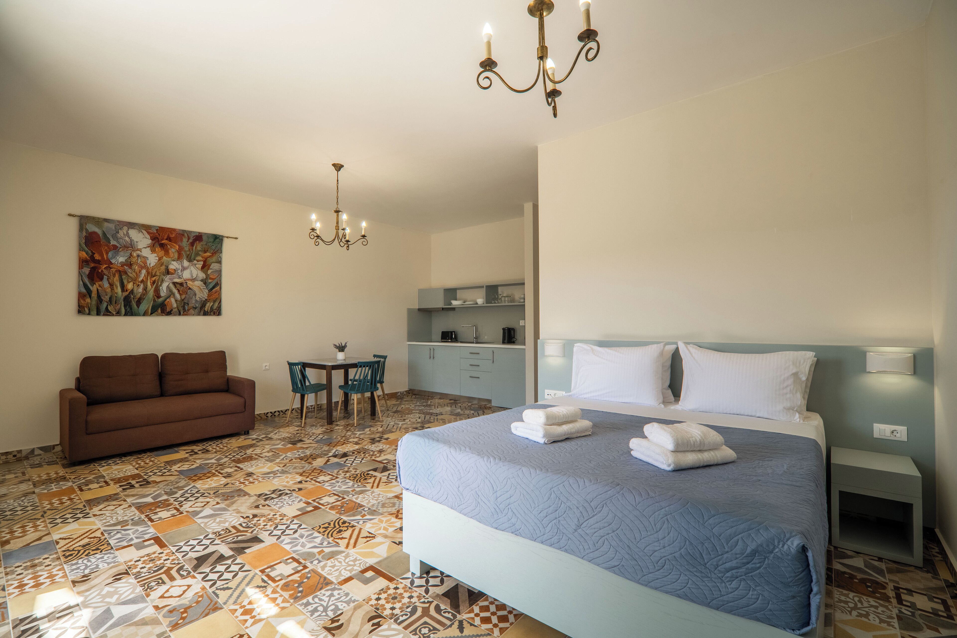 A hotel room with a large bed, a sofa, a dining table, and a kitchenette.