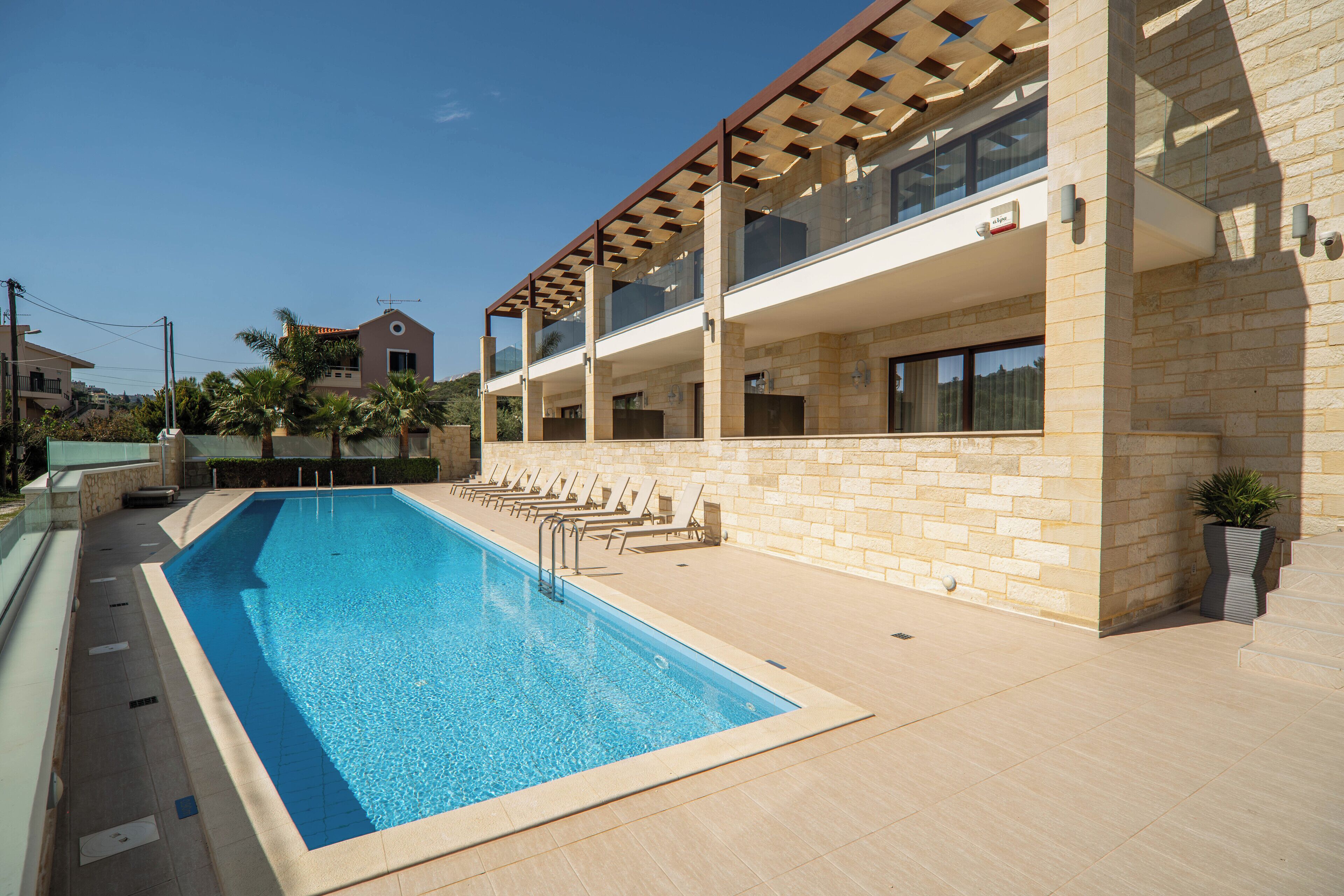 Un bâtiment moderne doté d’une piscine, de chaises longues et d’une façade en pierre.