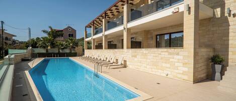 A modern building with a swimming pool, lounge chairs, and a stone facade.