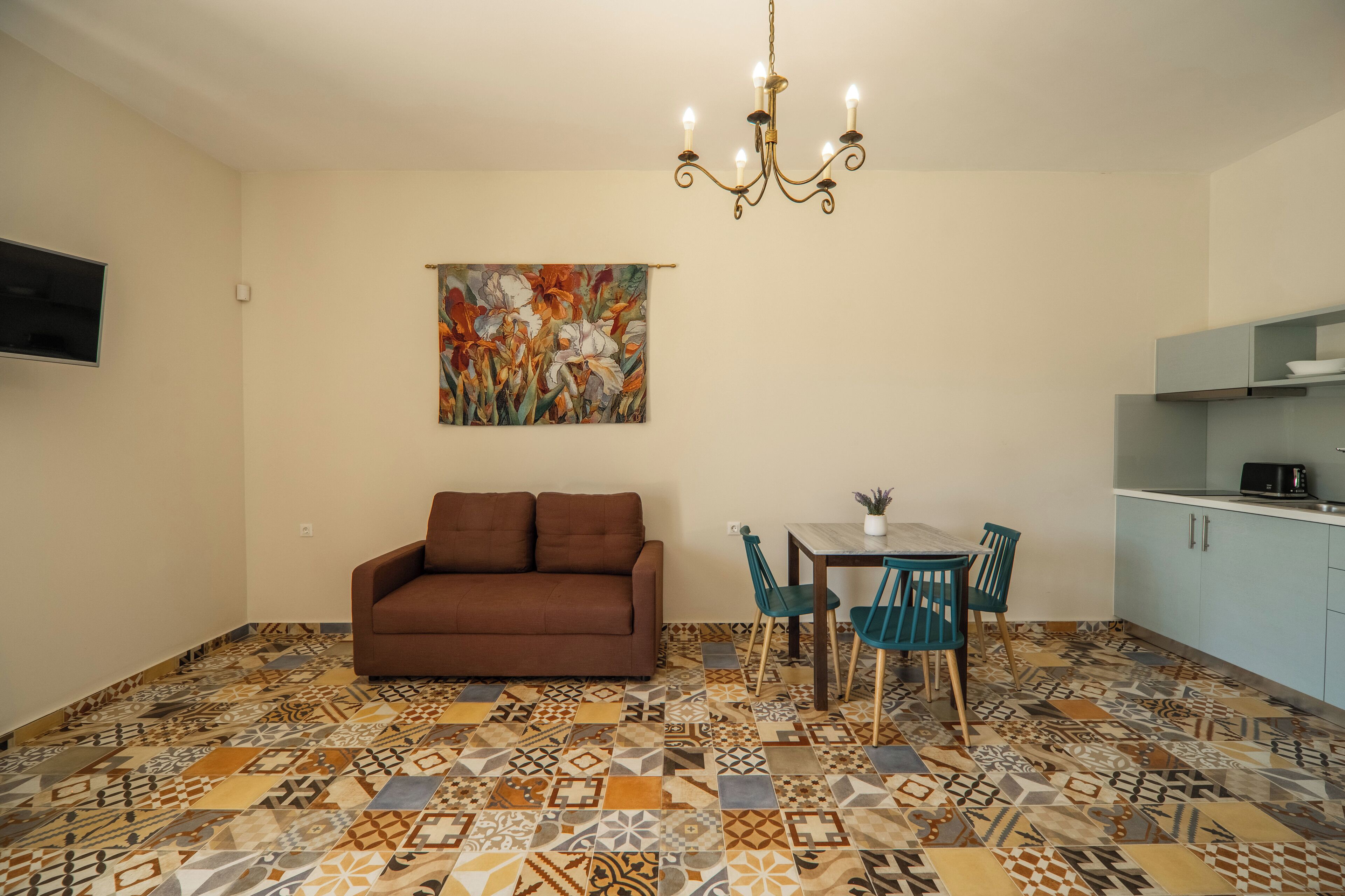 A living room with a brown sofa, a dining table with chairs, a chandelier, and a colorful abstract painting on the wall.