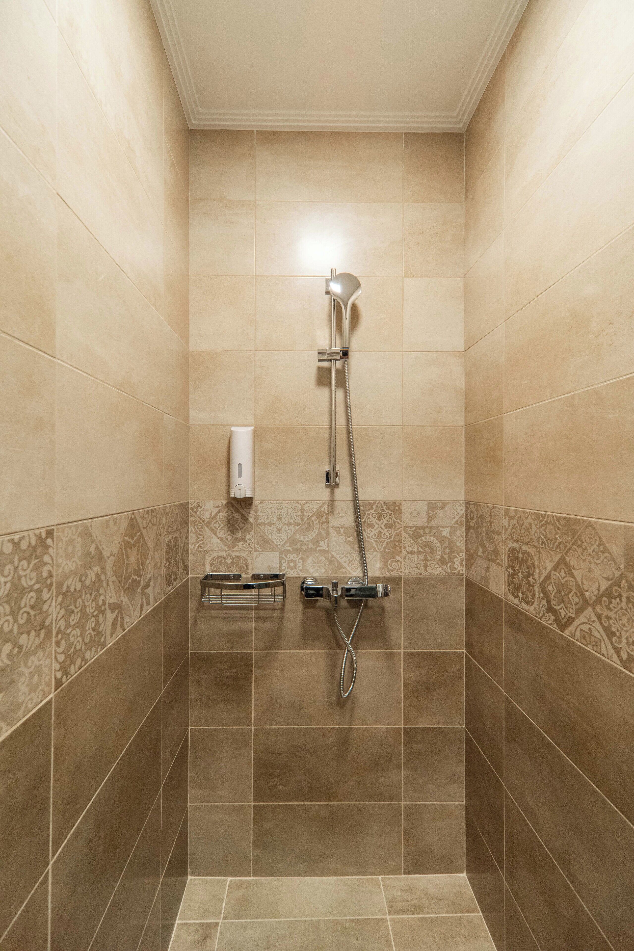 A shower with a handheld showerhead and a wall-mounted soap dispenser.