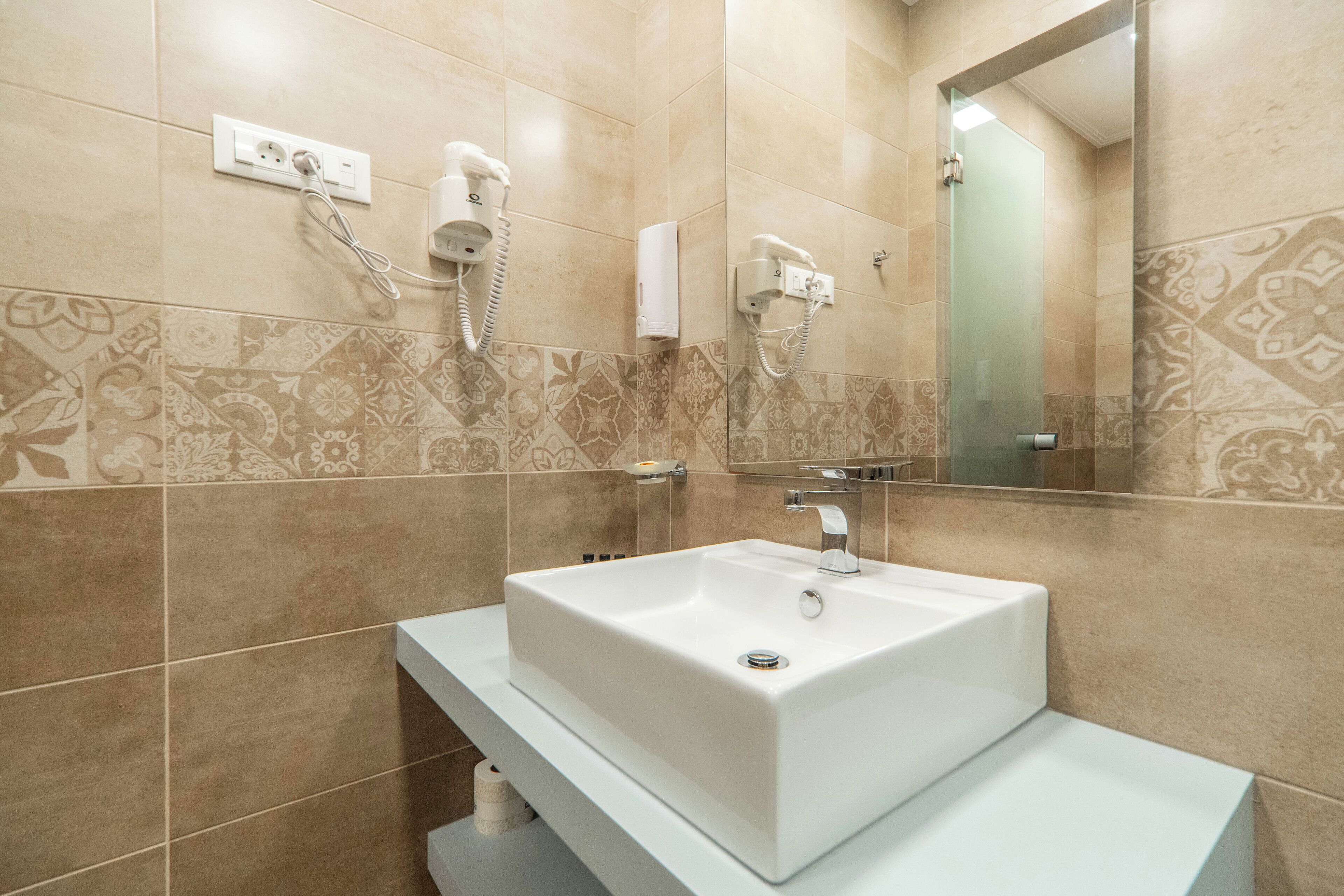 Un baño moderno con un lavamanos blanco, dos secadores de pelo montados en la pared y un espejo grande.