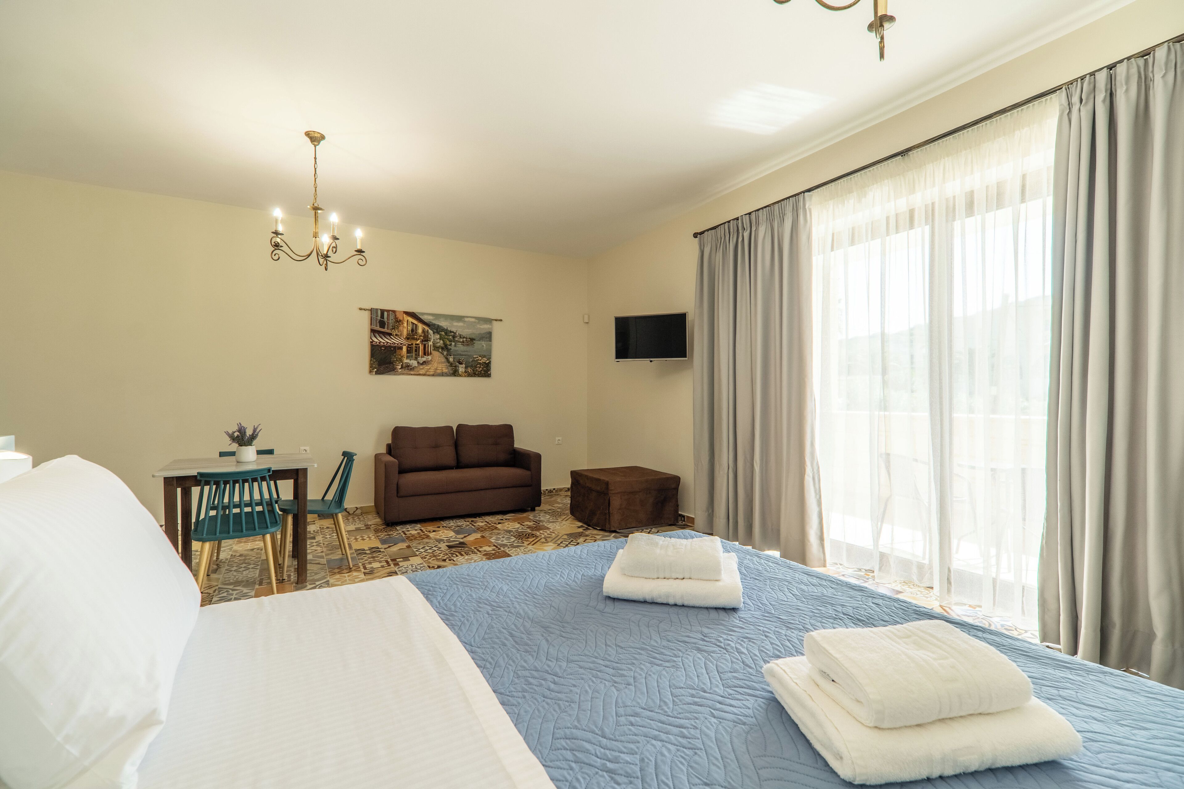 A hotel room with a bed, a desk, a sofa, a TV, and a window with curtains.
