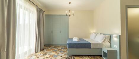 Un dormitorio con piso estampado, cama con cubierta azul, mesita de noche, armario y candelabro.