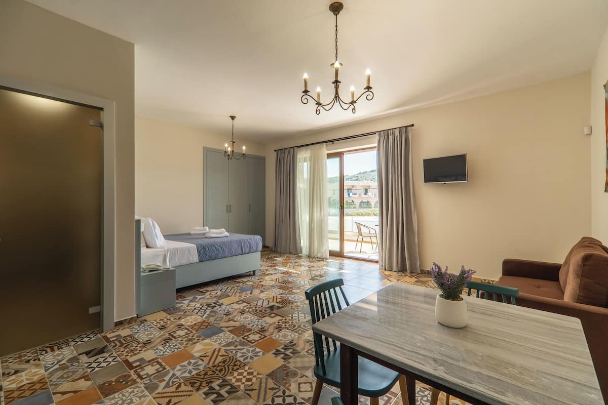 A hotel room with a bed, a dining table, a sofa, a TV, and a view of the outside.