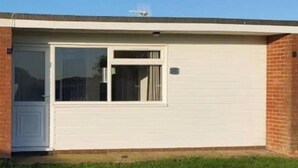 Une maison de plain-pied avec une porte de garage blanche, une petite fenêtre avec des rideaux et une façade en briques.