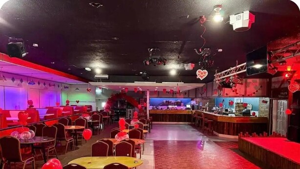 Un restaurant à l’éclairage rouge et violet, avec des tables décorées de ballons et un espace bar.