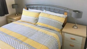 Un lit avec une literie à motifs, une tête de lit en métal, des tables de chevet avec des lampes et un mur sobre.