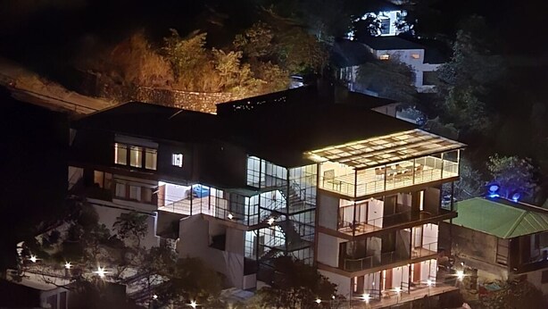 A modern multi-story building with large windows and a balcony area, surrounded by trees and a well-lit outdoor space. - Gurugram Resort Mussoorie (Mussoorie)