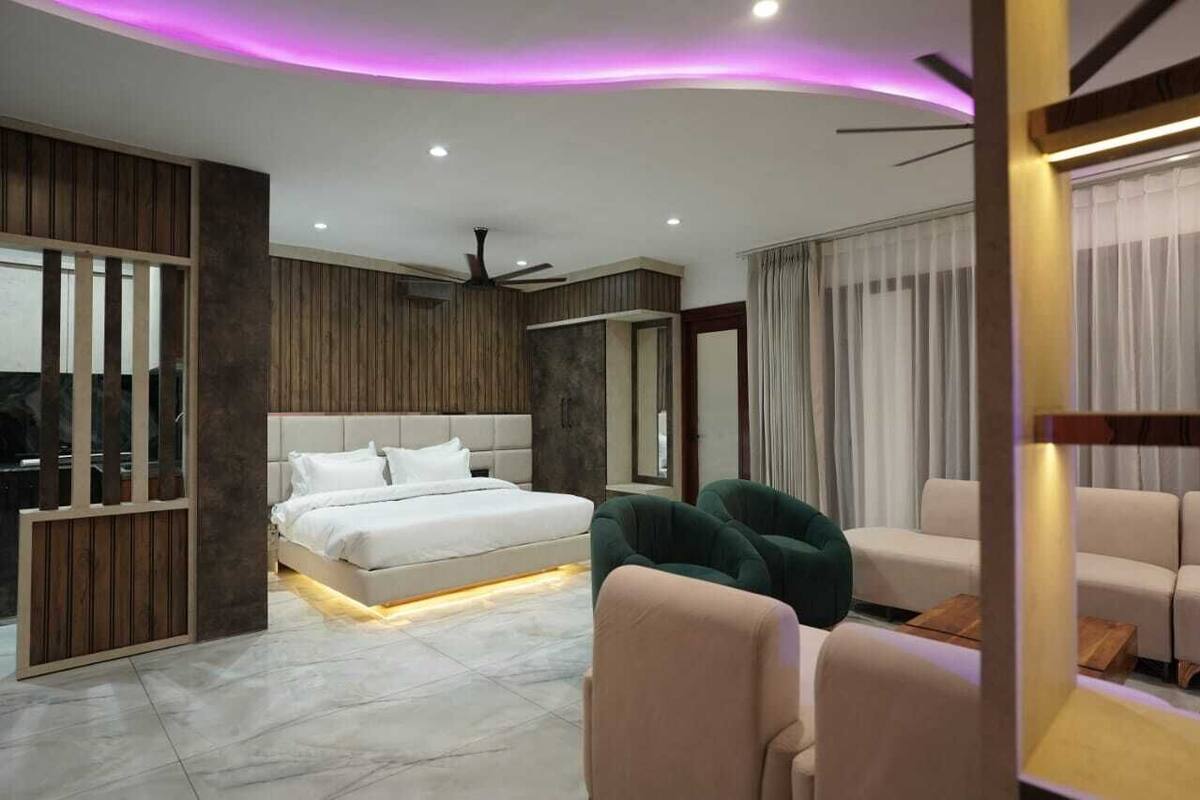 Egy modern hálószoba, amelyben található egy ágy, zöld karosszékek, egy kanapé és egy mennyezeti ventilátor.