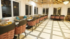 A dining area with long tables, cushioned chairs, and large windows. - Gurugram Resort Mussoorie (Mussoorie)