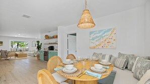 Un coin repas avec une table ronde dressée pour quatre personnes, entourée de chaises en osier et d’un canapé.