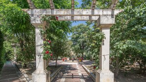 Un arco de piedra con un camino empedrado que atraviesa un jardín con árboles y flores.